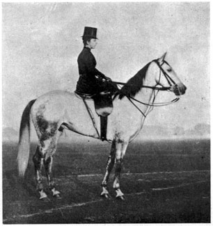 Woman seated side-saddle on a grey horse.